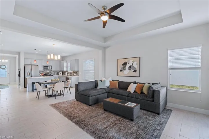 Living room featuring ceiling fan with notable chandelier, plenty of natural light, and a raised ceiling