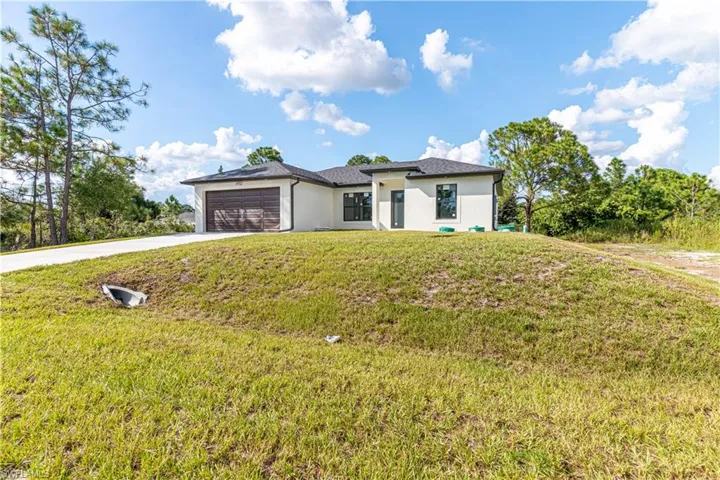 View of front facade with driveway, stucco siding, a front lawn, and an attached garage