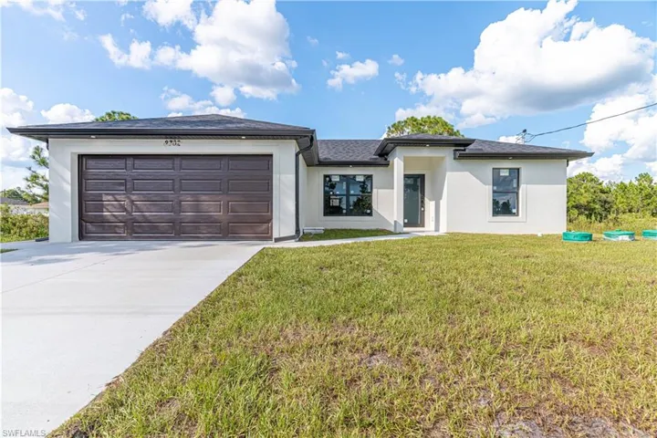 Prairie-style home with stucco siding, a front lawn, a garage, and concrete driveway