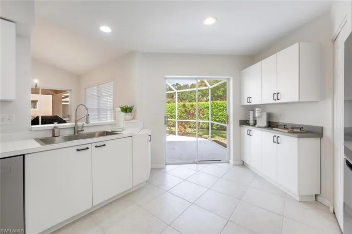 Kitchen with lofted ceiling, white cabinets, sink, and light tile patterned floors