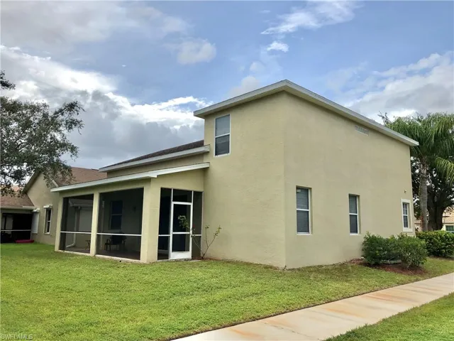 Rear view of house with stucco siding, a lawn, and a sunroom