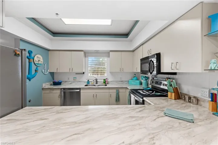 Kitchen featuring sink, a raised ceiling, backsplash, light stone countertops, and appliances with stainless steel finishes