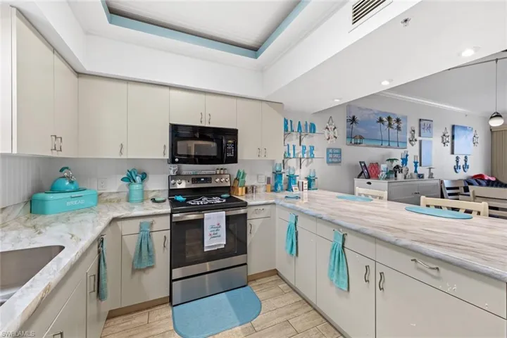 Kitchen featuring a raised ceiling, stainless steel electric range, crown molding, light stone countertops, and sink
