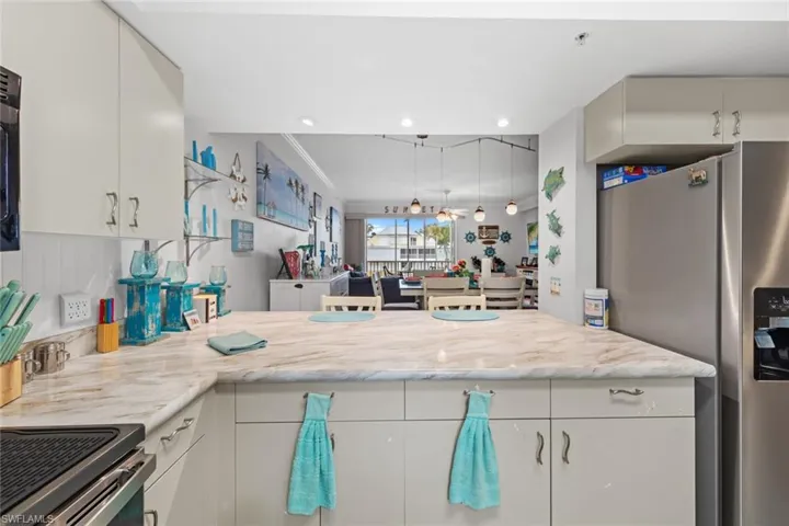 Kitchen with light stone countertops, white cabinetry, crown molding, and stainless steel refrigerator with ice dispenser