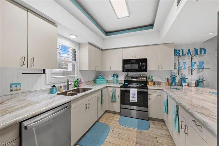 Kitchen featuring sink, stainless steel appliances, light stone counters, and a tray ceiling