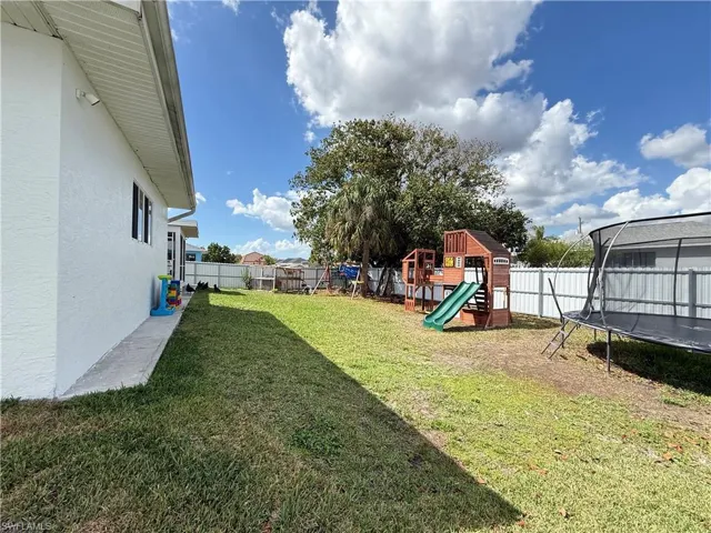 Fenced backyard featuring a trampoline and a playground