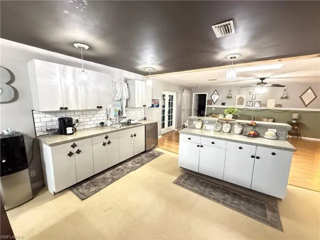 Kitchen featuring decorative light fixtures, backsplash, dishwasher, white cabinets, and a center island