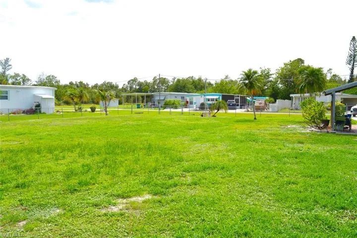 Expansive green lawn with visible perimeter fencing and mature palm trees