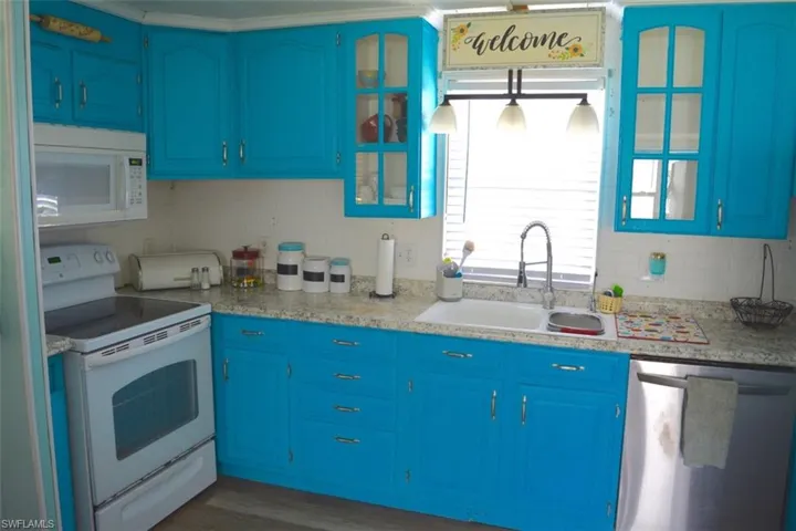 Kitchen featuring bright blue cabinetry with brushed nickel hardware, white appliances, a double basin sink, and a stainless steel dishwasher