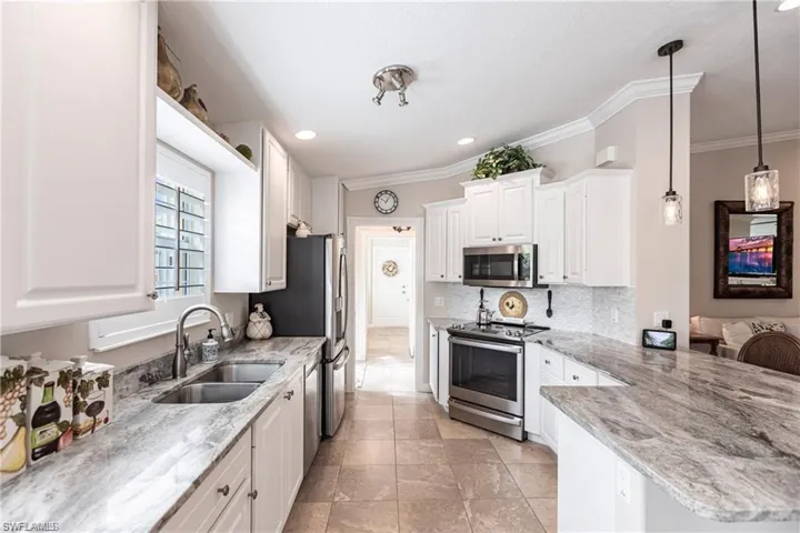Kitchen featuring sink, white cabinetry, stainless steel appliances, light stone countertops, and decorative light fixtures
