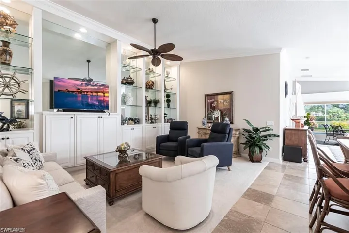 Tiled living room featuring built in features, ornamental molding, and ceiling fan
