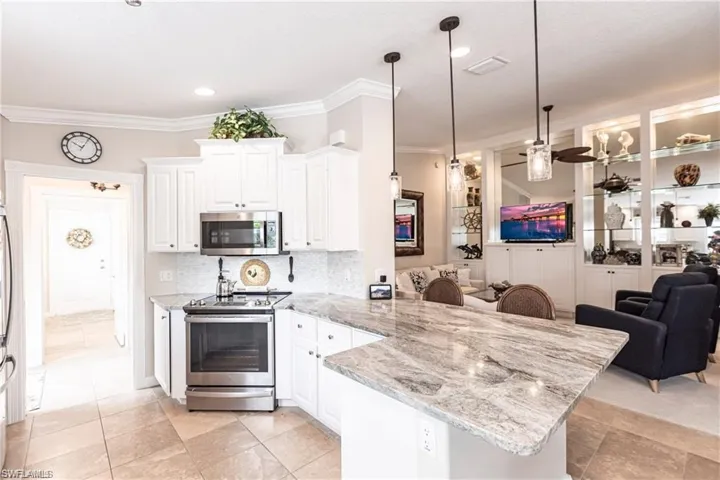 Kitchen with pendant lighting, tasteful backsplash, white cabinetry, kitchen peninsula, and stainless steel appliances