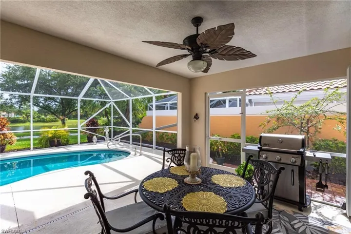 View of swimming pool with grilling area, ceiling fan, glass enclosure, and a patio area