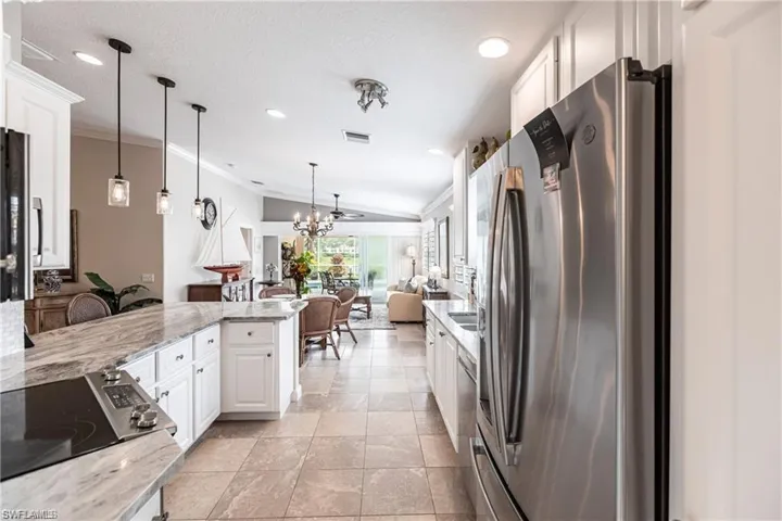 Kitchen featuring white cabinetry, stainless steel fridge, light stone countertops, and pendant lighting