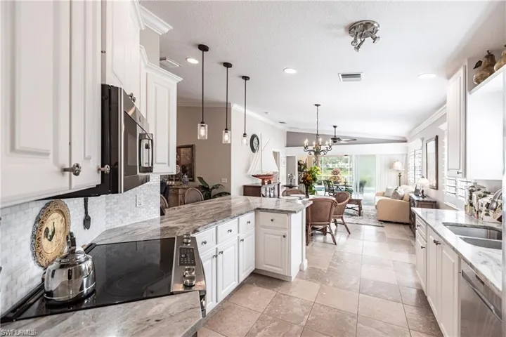 Kitchen featuring sink, white cabinetry, light stone counters, hanging light fixtures, and stainless steel appliances
