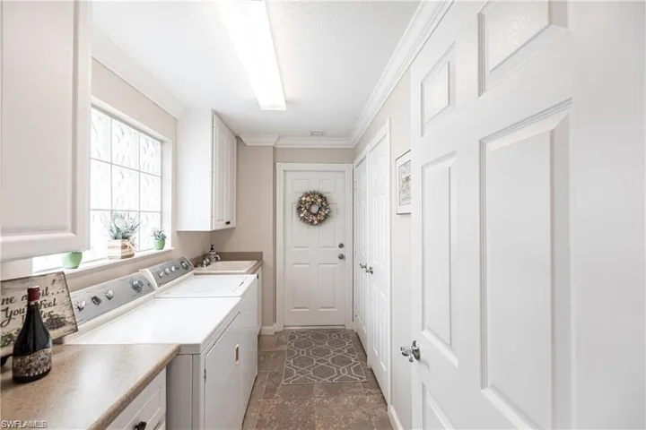 Clothes washing area with sink, crown molding, cabinets, a textured ceiling, and washing machine and dryer
