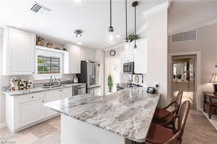 Kitchen featuring pendant lighting, sink, appliances with stainless steel finishes, white cabinetry, and kitchen peninsula
