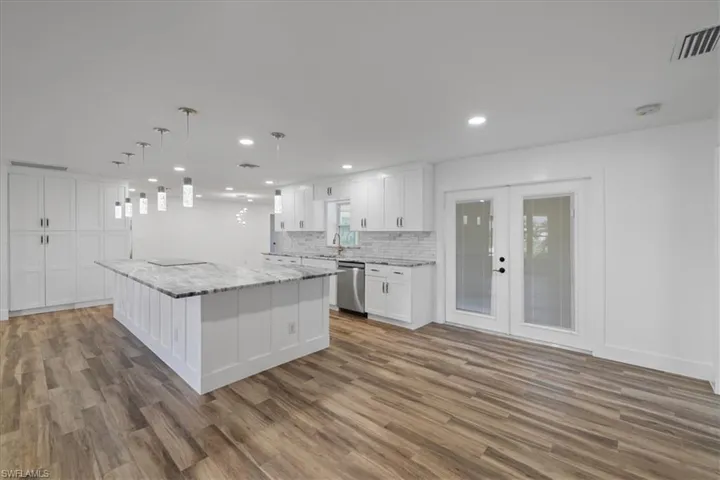 Kitchen with a kitchen island, white cabinetry, french doors, light stone countertops, and decorative light fixtures