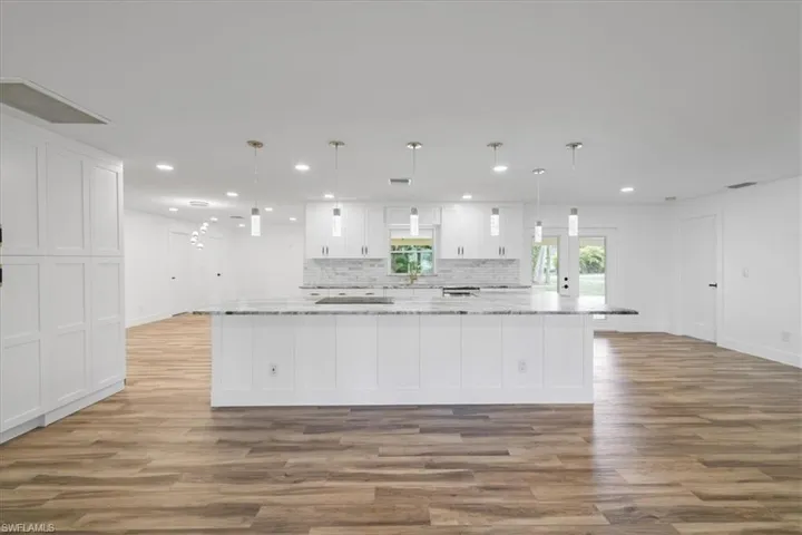 Kitchen featuring white cabinetry, decorative light fixtures, a large island with sink, light stone countertops, and tasteful backsplash