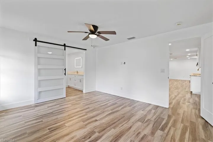 Master bedroom with a barn door, light wood-type flooring, ensuite bathroom, and ceiling fan