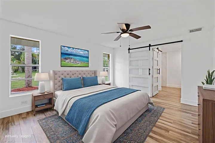 MasterBedroom virtualy staged with a barn door, multiple windows, light wood-style floors, and a ceiling fan