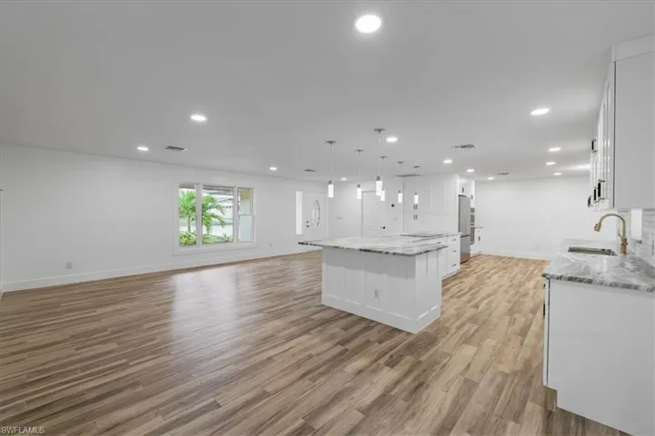 Kitchen with white cabinetry, open floor plan, light stone countertops, light wood-type flooring, and recessed lighting