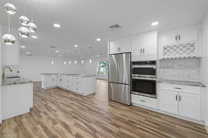 Kitchen featuring decorative light fixtures, white cabinetry, appliances with stainless steel finishes, light stone countertops, and recessed lighting