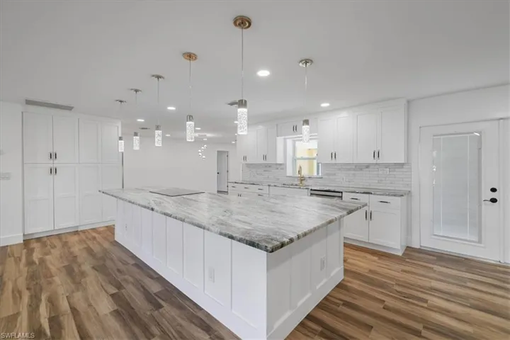 Kitchen featuring pendant lighting, white cabinets, light stone countertops, a large island, and recessed lighting
