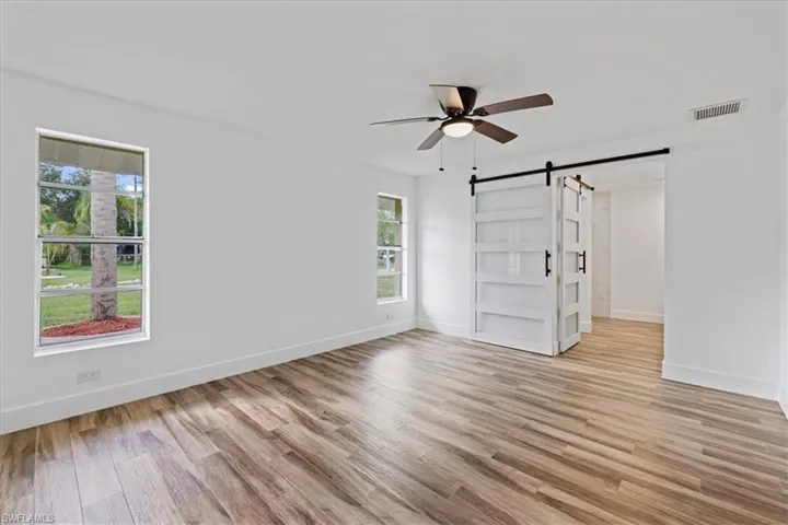 Master Unfurnished bedroom with a barn door, light wood-style floors, and ceiling fan