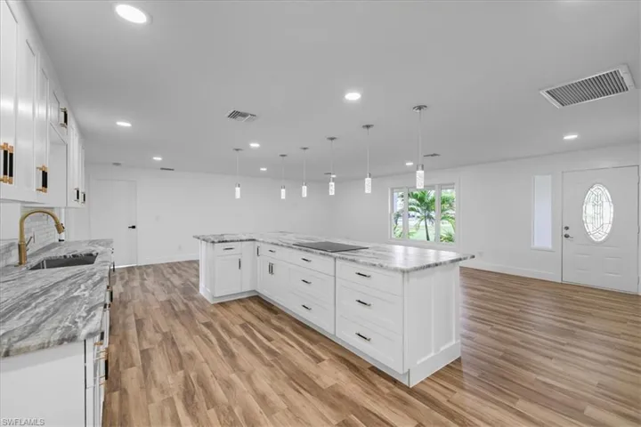 Kitchen with white cabinets, decorative light fixtures, light stone counters, light wood-style floors, and stainless steel dishwasher
