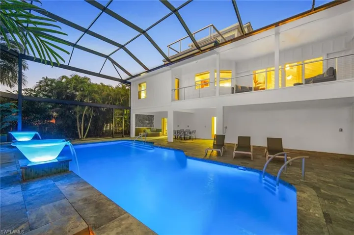 Pool at dusk with an infinity fountains, a lanai, and a patio