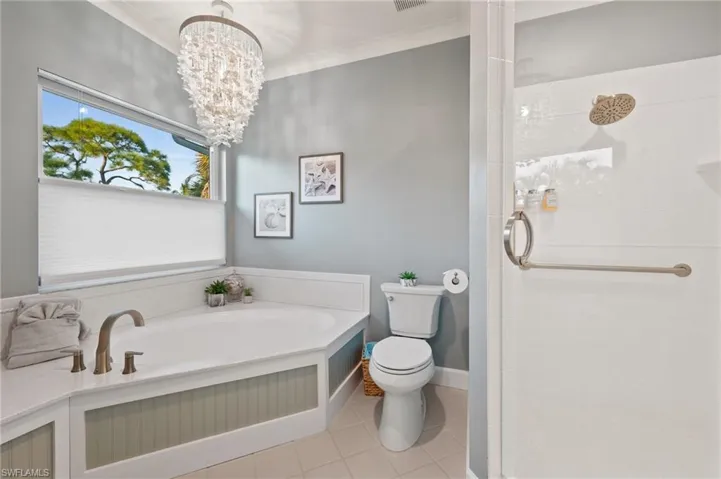 Full bath featuring a stall shower, light tile patterned floors, a bath, a chandelier, and crown molding