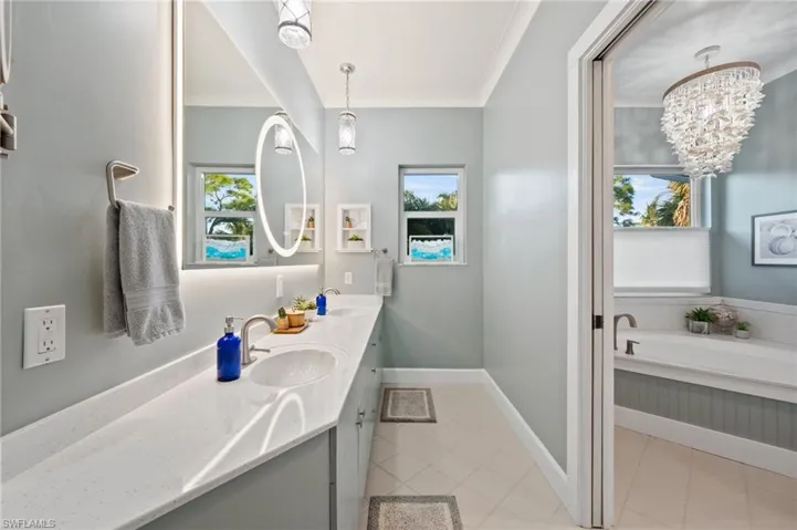 Bathroom with double vanity, a chandelier, crown molding, and a soaker tub with separate shower stall