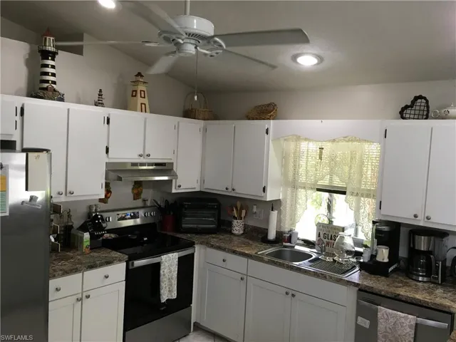 Kitchen featuring white cabinetry, stone-look countertops, stainless steel appliances, a double basin sink, and a ceiling fan with integrated lighting