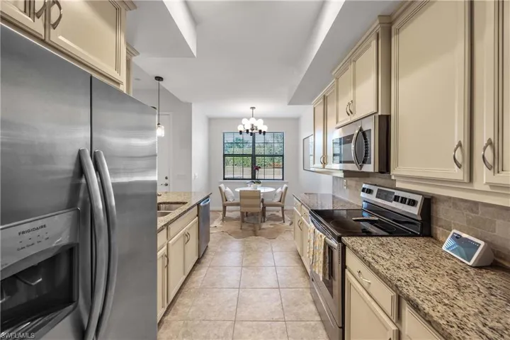 Kitchen featuring light stone counters, tasteful backsplash, light tile patterned floors, pendant lighting, and stainless steel appliances