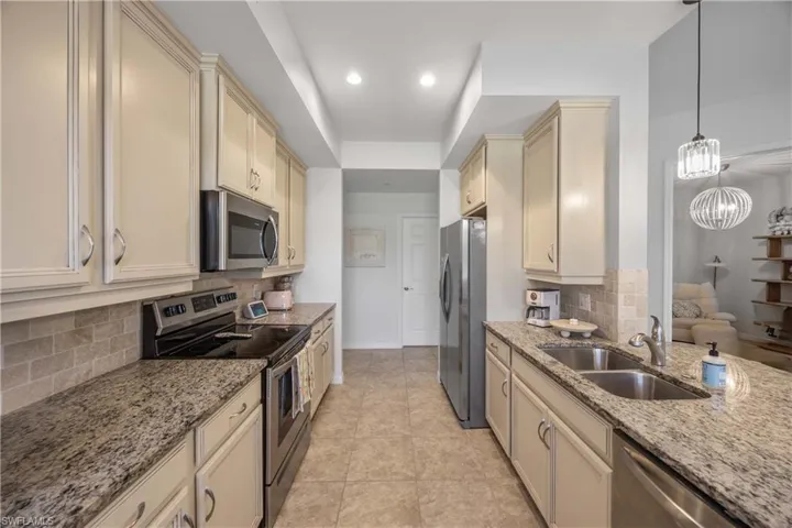 Kitchen featuring sink, appliances with stainless steel finishes, hanging light fixtures, light stone countertops, and cream cabinetry