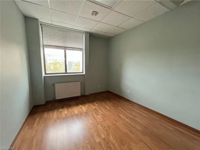 Room featuring wood-finish flooring, a suspended acoustic tile ceiling, and neutral-toned walls
