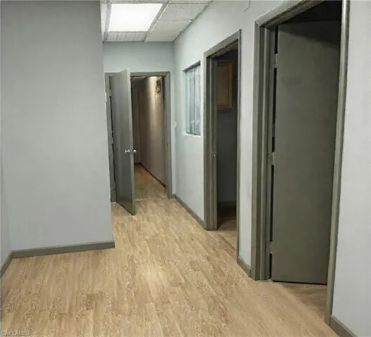 Hallway featuring wood-finish flooring, light grey walls, and multiple doorways with dark trim