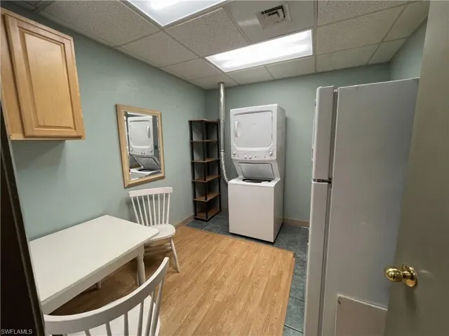 Compact utility space featuring a stacked washer and dryer unit, wood-finish flooring, and a drop ceiling with fluorescent lighting