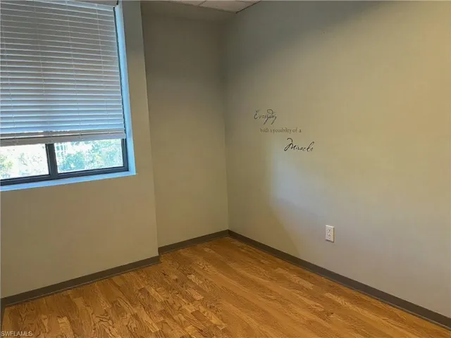 Room featuring wood-finish flooring, a window with horizontal blinds, and a neutral wall color