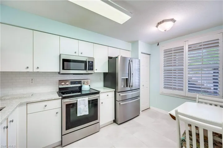 Kitchen with appliances with stainless steel finishes, white cabinetry, decorative backsplash, and light stone countertops