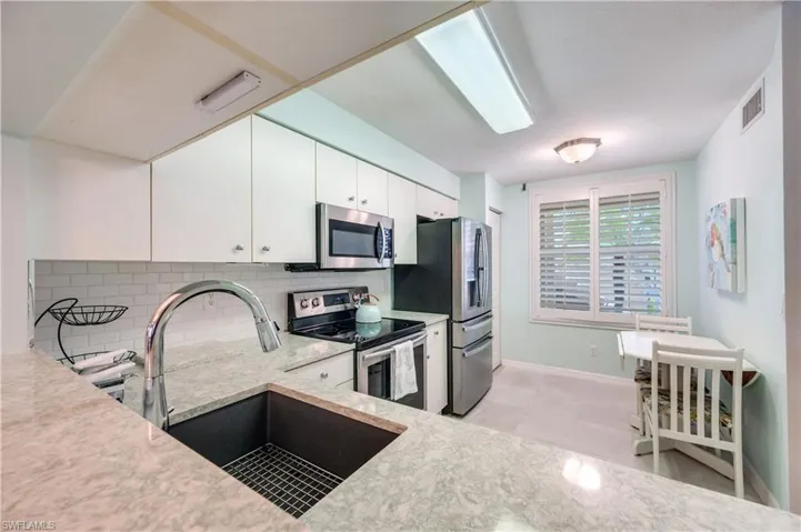 Kitchen with appliances with stainless steel finishes, white cabinetry, tasteful backsplash, light stone countertops, and light tile patterned floors