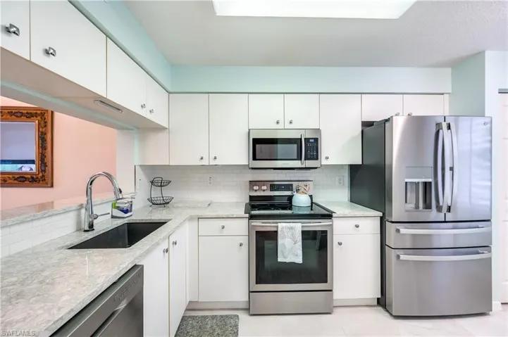 Kitchen with stainless steel appliances, decorative backsplash, light stone countertops, and white cabinets
