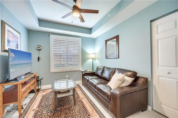 Living room with a raised ceiling, a ceiling fan, and plenty of natural light