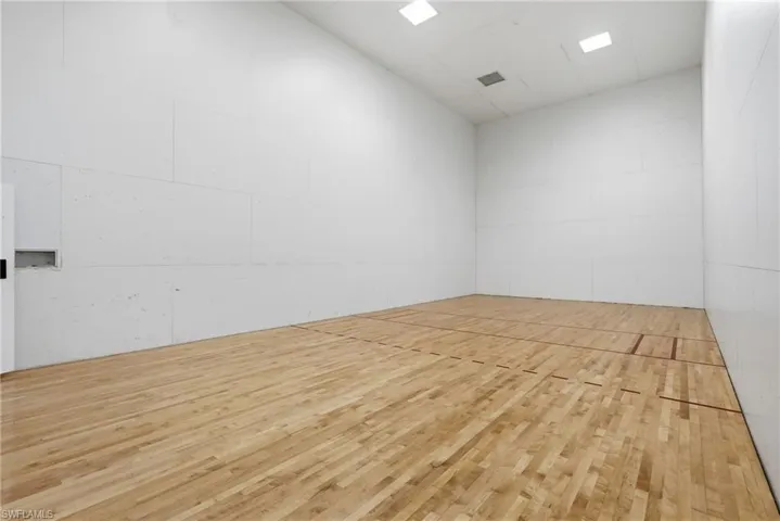 Dedicated indoor court featuring light wood-finish flooring with court markings, white paneled walls, and recessed ceiling lighting