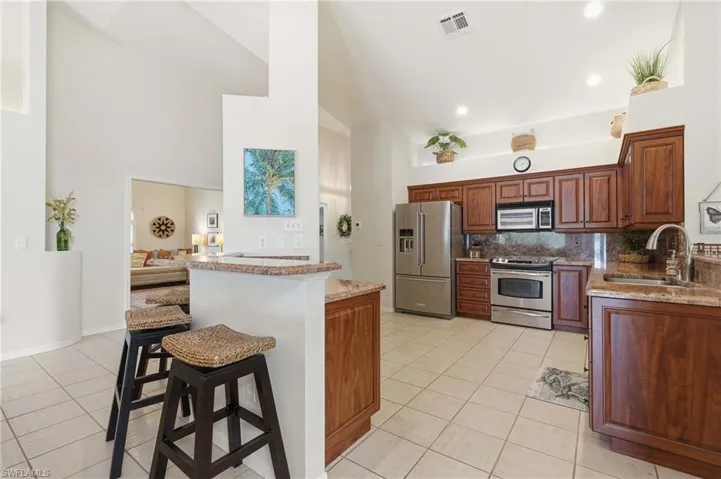Kitchen featuring stainless steel appliances, wood-finish cabinetry, granite countertops, and tile flooring