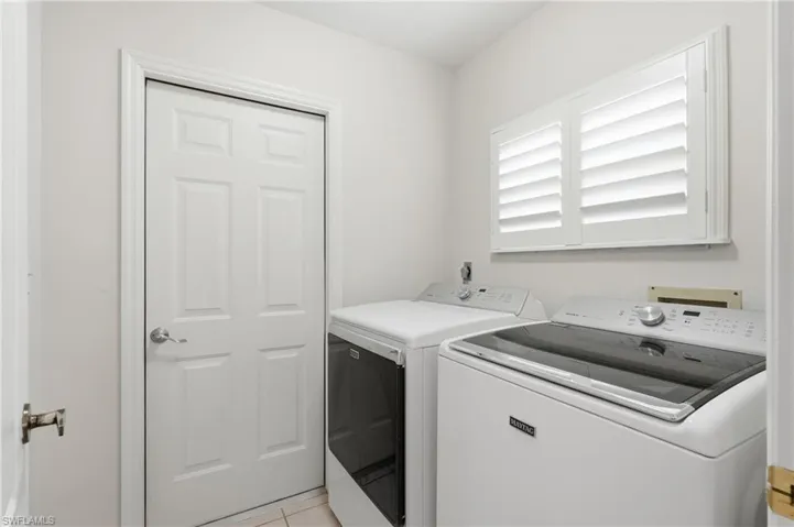 Dedicated laundry space featuring white plantation shutters and tiled flooring