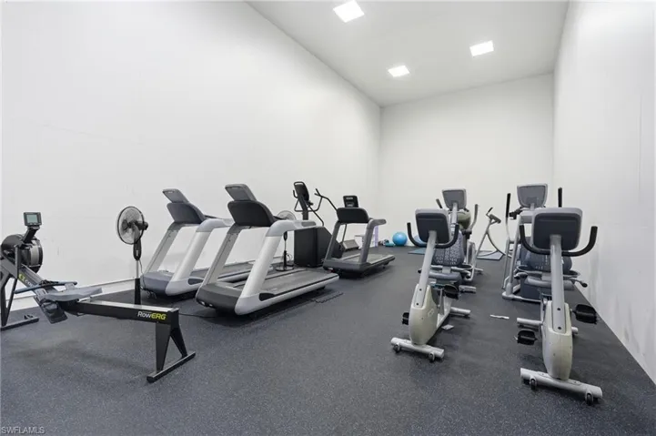 Dedicated fitness room featuring resilient rubber flooring, recessed ceiling lighting, and stark white wall finishes
