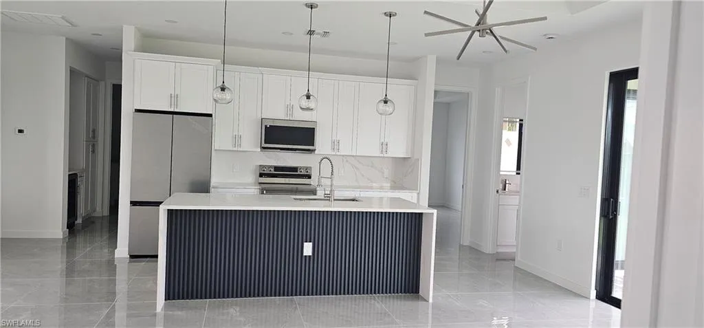 Kitchen with stainless steel appliances, light stone countertops, a kitchen island with sink, pendant lighting, and white cabinetry