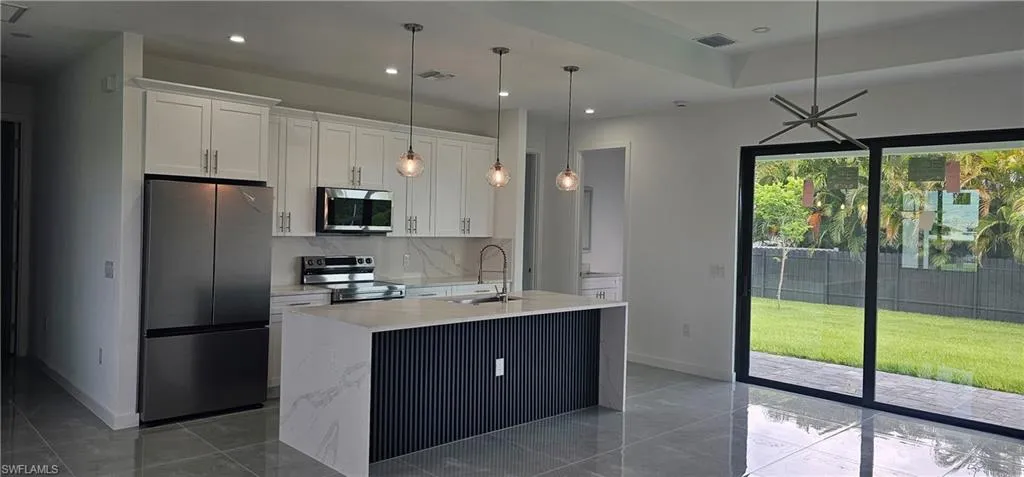 Kitchen with appliances with stainless steel finishes, white cabinetry, light stone countertops, decorative light fixtures, and a center island with sink